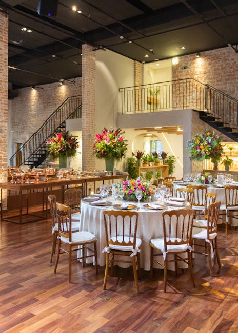 Elegant event space with polished wooden flooring and exposed brick walls illuminated by warm lighting. In the foreground, a round table is dressed with a white tablecloth, set with fine china, crysta