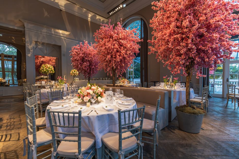 An elegant interior setting featuring a wedding floral arrangement in Kensington Palace Road. The room is decorated with three large, vibrant pink cherry blossom trees in substantial pots, placed alon